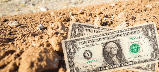 Dollar bills laying on an unpaved dirt industrial road