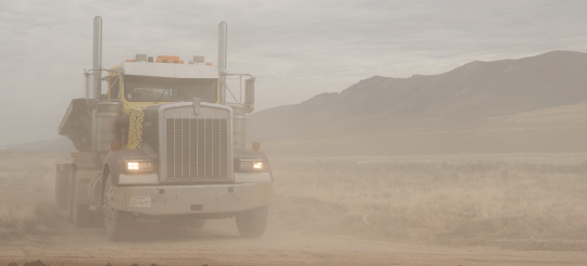 Heavy-duty semi truck driving through a dust cloud on an unpaved road