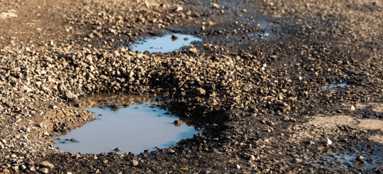 Water-filled potholes on an unpaved gravel road