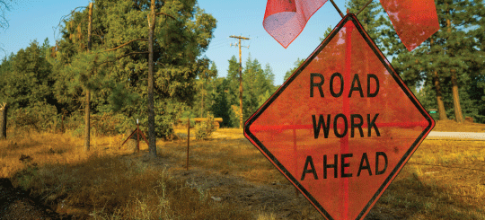 Orange road work ahead sign alongside an unpaved road in California